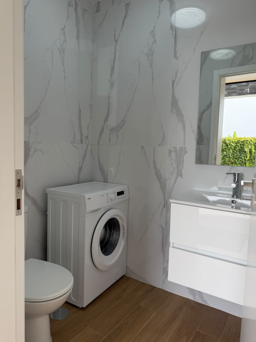 Banheiro moderno com máquina de lavar branca, sanitário, pia e azulejos com efeito mármore na villa Sunshine 85 House em Ribeira Brava
