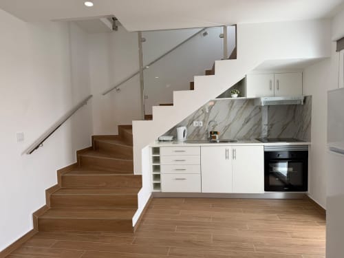 Cozinha moderna com armários brancos e bancada em mármore sob escada de madeira na villa Sunshine 85 House, Madeira