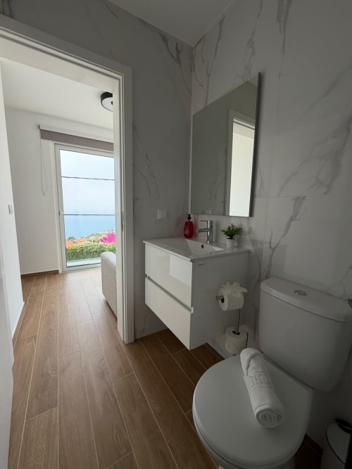 Banheiro moderno da villa Sunshine 85 House, Madeira, com paredes em mármore, móvel branco, espelho, sanitário e vista para o mar
