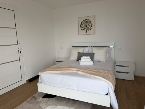Quarto moderno na villa Sunshine 85 House, Ribeira Brava com cama branca, piso em madeira e arte com vista para o mar.