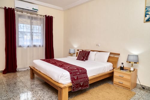 Chambre supérieure à l'Hôtel Yakro à Yamoussoukro avec lit en bois, draps blancs, accents bordeaux et vue sur la ville
