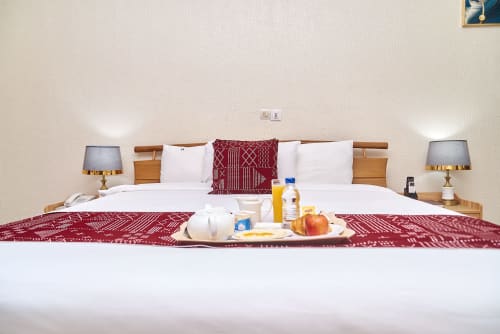 Chambre supérieure de l'Hôtel Yakro Yamoussoukro avec lits jumeaux, parure bordeaux, amenités de bienvenue et vue sur la ville