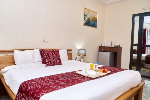 Spacieuse chambre supérieure à l'Hôtel Yakro à Yamoussoukro avec draps blancs, lit en bois, accents bordeaux et vue sur la ville