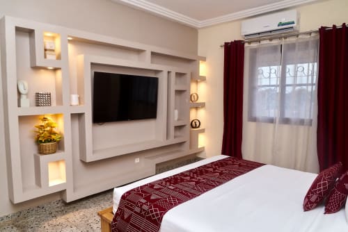 Chambre supérieure moderne à l'Hôtel Yakro à Yamoussoukro avec télévision écran plat, éclairage ambiant et accents bordeaux