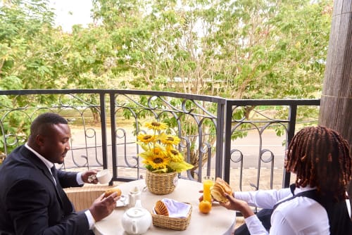 Deux clients dînent sur un balcon fleuri à l'Hôtel Yakro de Yamoussoukro, entourés d'arbres et de vues urbaines