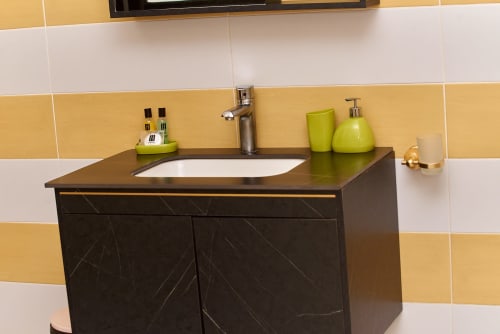 Meuble vasque moderne avec armoire noire et lavabo blanc à l'Hôtel Yakro, dosseret en carreaux à rayures jaunes et blanches