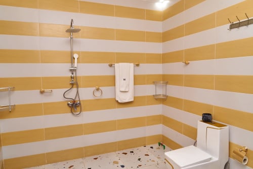 Salle de bain moderne à l'Hôtel Yakro avec carrelage rayé or et blanc, douche à effet pluie et porte-serviettes chauffant à Yamoussoukro