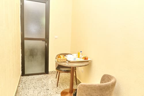 Chambre supérieure de l'Hôtel Yakro à Yamoussoukro avec table ronde en bois, fauteuil et porte en verre dépoli