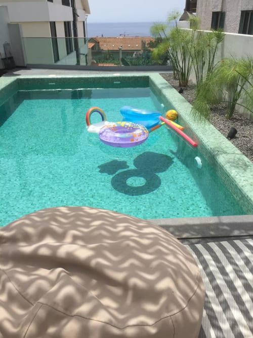 Piscina turquesa com flutuadores coloridos nas Villas Simone, Portugal, vista para o oceano ao fundo