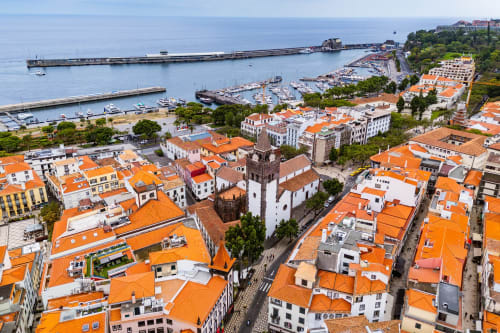 Vista aérea da cidade costeira de Lisboa com edifícios de telhados laranja, marina e torre histórica sobre o Atlântico