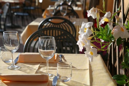 Tavolo preparato presso Holiday Suites Pesaro con bicchieri d'acqua, fiori bianchi e sedie nere nella sala da pranzo