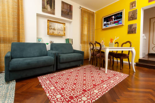 Luminoso salotto di lusso a Venezia con divano teal, tappeto rosso decorato, parete gialla e zona pranzo