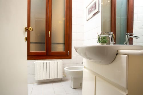 Bagno moderno in lussuoso loft veneziano con lavabo a parete, toilette, radiatore riscaldante e specchio con cornice in legno