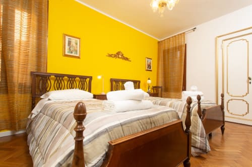 Lussuosa camera da letto a Venezia con pareti giallo brillante, letti gemelli in legno, tende dorate e pavimenti in legno massello al Royal Rialto