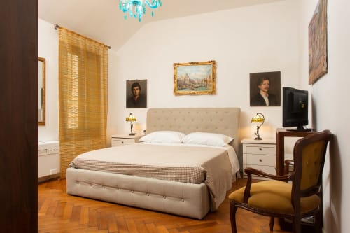 Lussuosa camera da letto in appartamento veneziano con letto capitonné color crema, scrivania in legno, opere d'arte e pavimenti in cotto vicino al Canal Grande.
