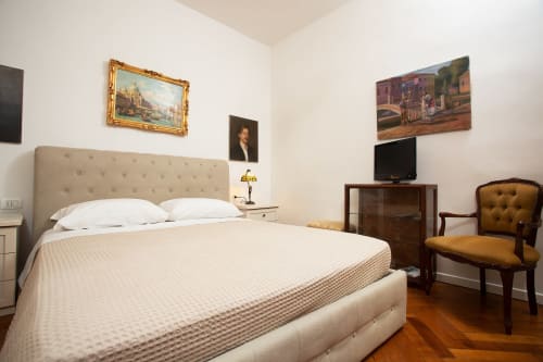 Camera da letto elegante in Luxury Loft Venezia con testiera trapuntata beige, biancheria bianca, mobili in legno, TV e opere d'arte classica