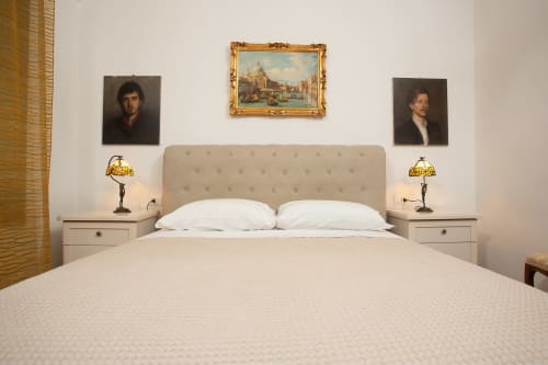 Elegante camera da letto in appartamento veneziano con letto rivestito in beige, cuscini bianchi, comodini con lampade in ottone e dipinti ritrattistici.
