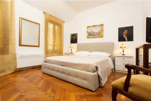 Lussuosa camera da letto a Venezia con letto in velluto crema, cornici dorate, pavimenti in legno e vista sulla città