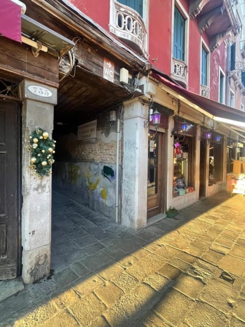 Affascinante ingresso di una strada veneziana con portale decorato, facciata rossa e caldo illuminamento serale nella storica Italia