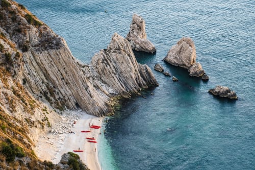 Spettacolari scogliere costiere con acque turchesi e barche rosse sulla spiaggia di Pesaro, Italia