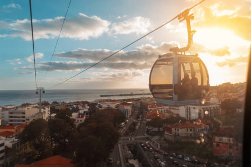 Teleférico ascendendo acima da costa de Lisboa com mar, edifícios e pôr do sol ao fundo