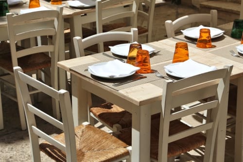 Sedie in legno bianco e tavolo apparecchiato con piatti e bicchieri ambra al ristorante Holiday Suites di Pesaro