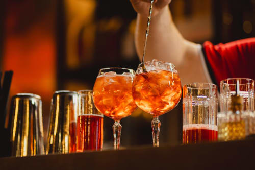 Barista versa Aperol Spritz a Holiday Suites Pesaro, con cocktail colorati e bicchieri da bar sul bancone