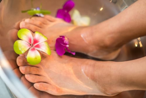 Piedi dell'ospite con fiori tropicali durante il trattamento spa di Holiday Suites Pesaro