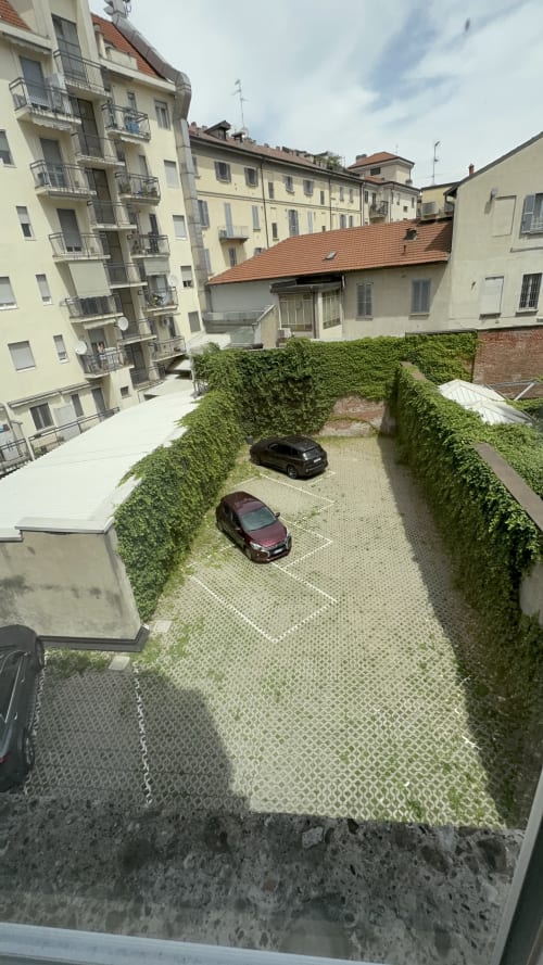 Area parcheggio della Porta Romana Suite Milano con due automobili, siepi e edifici residenziali circostanti