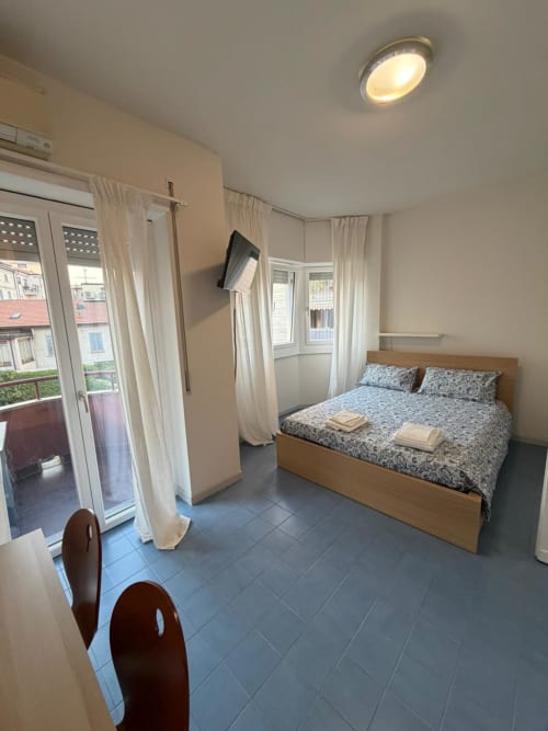 Luminoso monolocale a Porta Romana Suite Milano con letto in legno, finestre, balcone, TV e pavimenti in piastrelle blu