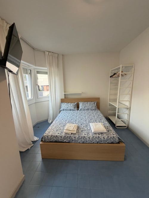 Camera luminosa della Porta Romana Suite Milano con letto in legno, biancheria a motivi, TV e armadio bianco
