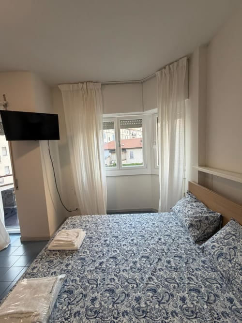 Camera luminosa con letto decorato, tende color crema, vista finestra, TV e arredamento moderno - Porta Romana Suite Milano