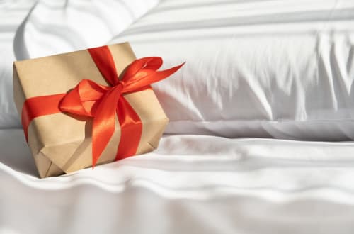 Gift-wrapped present with red bow on white bed at Holiday Suites hotel in Pesaro