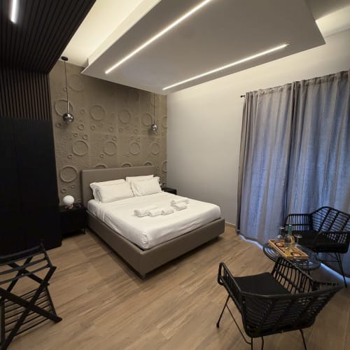 Camera moderna presso Eterna Suites Roma con letto matrimoniale, parete accent strutturata, luci ambientali al soffitto e sedute contemporanee