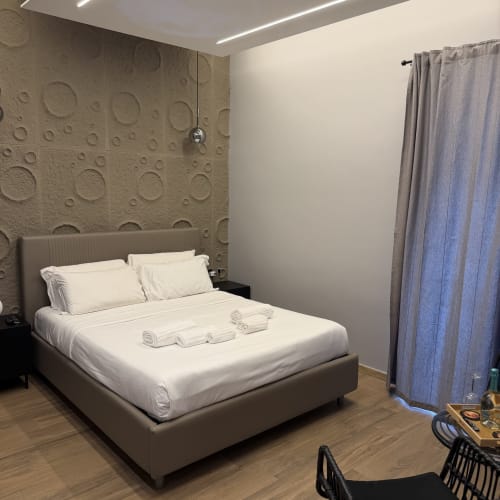 Camera moderna presso Eterna Suites Roma con letto imbottito grigio, biancheria bianca, parete in rilievo e tende blu