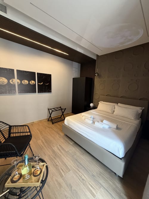 Camera suite moderna presso Eterna Suites Roma con letto matrimoniale, parete scura in contrasto, arte con fasi lunari, pavimentazione in legno e