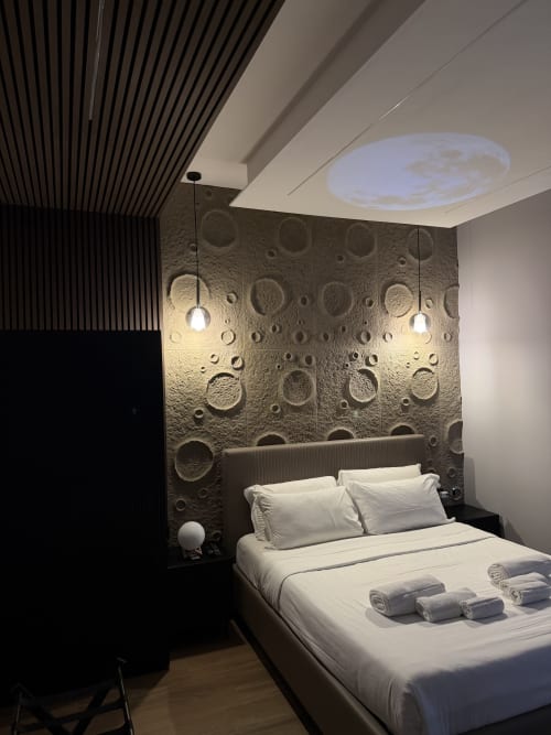 Camera Moon Suite presso Eterna Suites Roma con carta da parati a crateri lunari, biancheria bianca, luci a sospensione e vista città dal soffitto