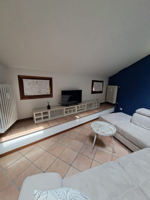 Ampio soggiorno dell'appartamento Aura presso Le Arche Verona con TV, mensole bianche, divani color crema e parete di accento blu navy