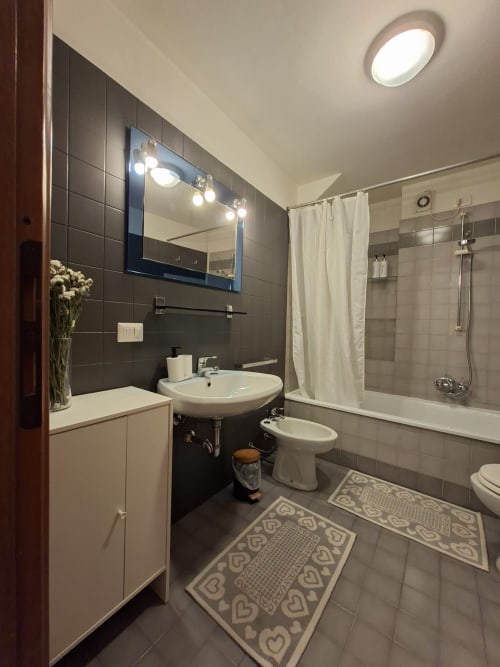 Moderno bagno con piastrelle scure, specchio illuminato, lavabo, wc, bidet e doccia nell'appartamento Le Arche Verona