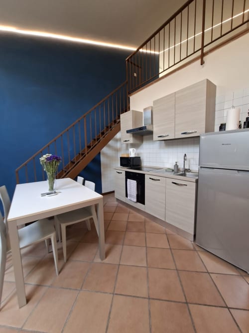 Cucina e zona pranzo moderne dell'appartamento Aura presso l'hotel Le Arche di Verona, con mobili bianchi, scala e accenti blu