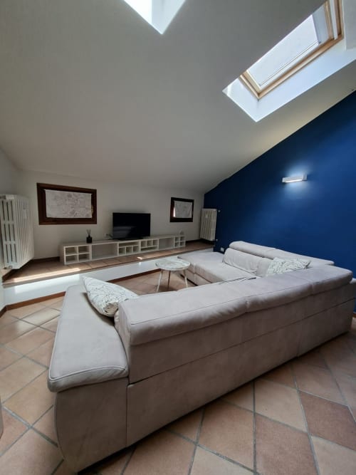 Moderno soggiorno di Le Arche apartment a Verona con divano a L, lucernario, parete blu e zona TV