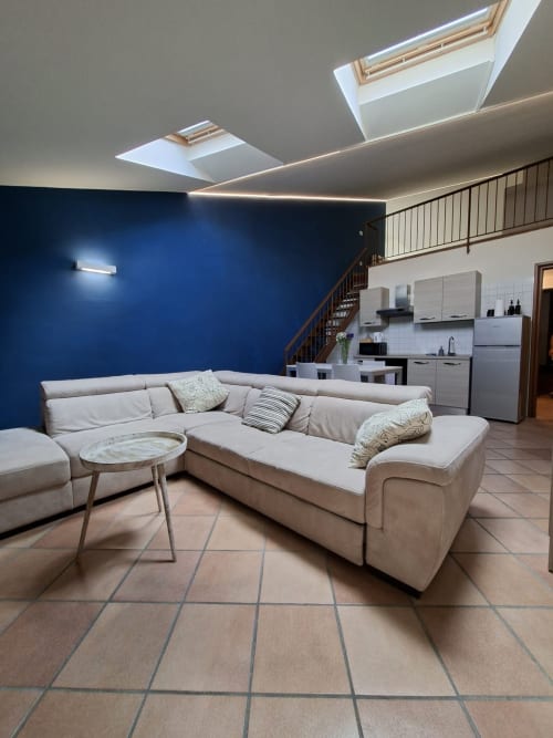 Moderno loft a Verona con divano componibile beige, parete blu, lucernario e cucina a vista