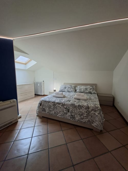 Luminosa camera da letto mansardata nell'appartamento Le Arche di Verona, con soffitti spioventi, lucernario, biancheria decorativa e pavimenti in cotto.