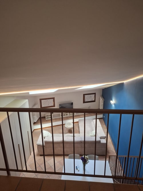 Camera soppalcata con vista sulla zona living dell'appartamento Aura all'hotel Le Arche di Verona, con ringhiere in legno e arredamento moderno