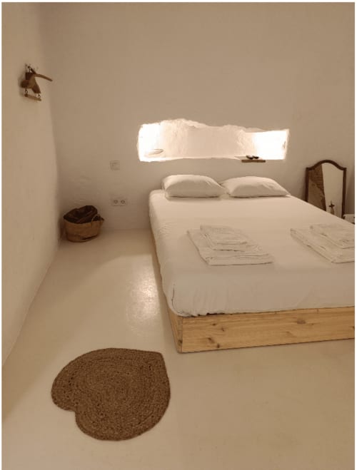 Quarto minimalista em Casas Velhinhas em Estremoz com cama branca, estrutura de madeira, tapete em forma de coração e luz natural brilhante