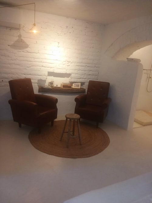 Aconchegante sala de estar no apartamento Casas Velhinhas com cadeiras bordô, tapete redondo e parede de tijolos brancos em Estremoz
