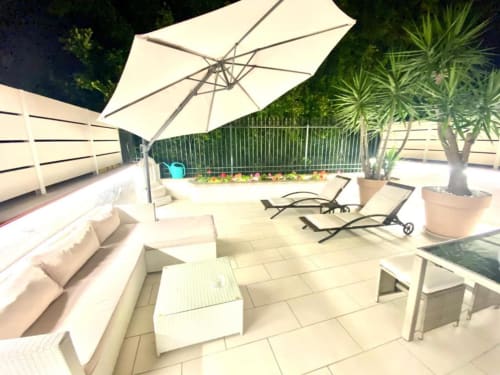 Terrazza degli Mottola Apartments a Tropea con ombrellone bianco, lettini relax, divano e vista sul giardino