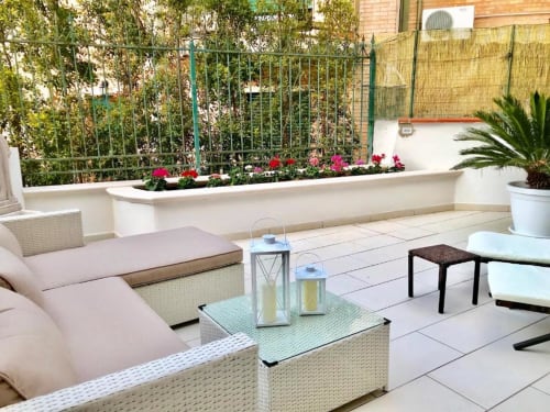 Area relax sulla terrazza degli Appartamenti Mottola a Tropea con mobili in vimini, cuscini rosa, fioriere fiorite e giardino
