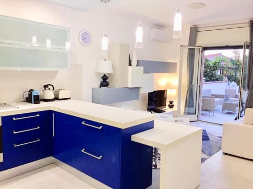Cucina moderna bianca e blu con isola negli Appartamenti Mottola di Tropea, con vista sulla terrazza e il giardino