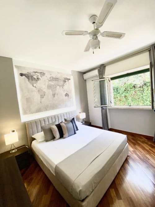 Camera luminosa presso gli Apartamenti Mottola a Tropea con letto bianco, ventilatore a soffitto, mappa mondiale, finestra con vista sul giardino e